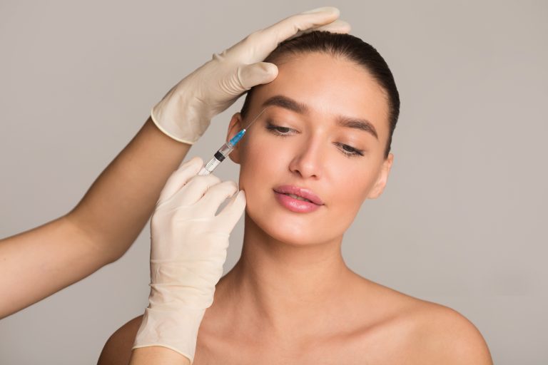 Plastic Surgery And Beauty Injection Concept. Young Woman Receiving Botox For Wrinkles, Isolated Over Studio Wall